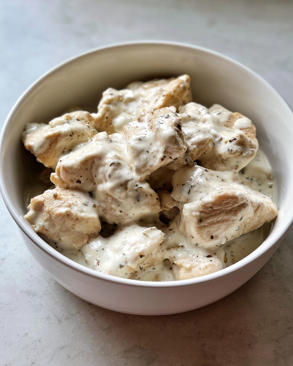 Close-up of bite-sized pieces of Easy Creamy Ranch Chicken coated in a thick, speckled white sauce, served in a white bowl.