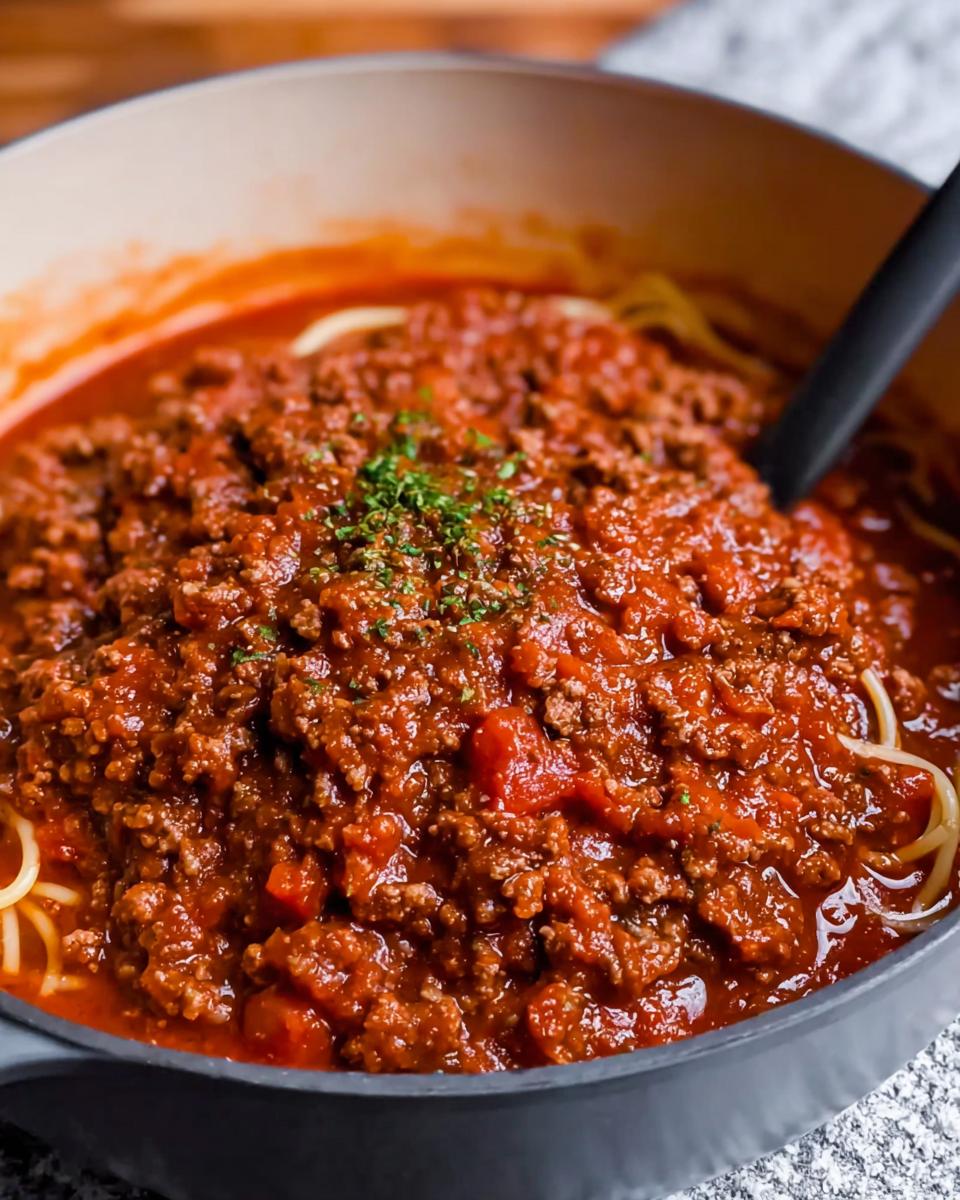 Close-up of Easy Weeknight Meat Sauce generously covering spaghetti noodles in a dark cooking pot.