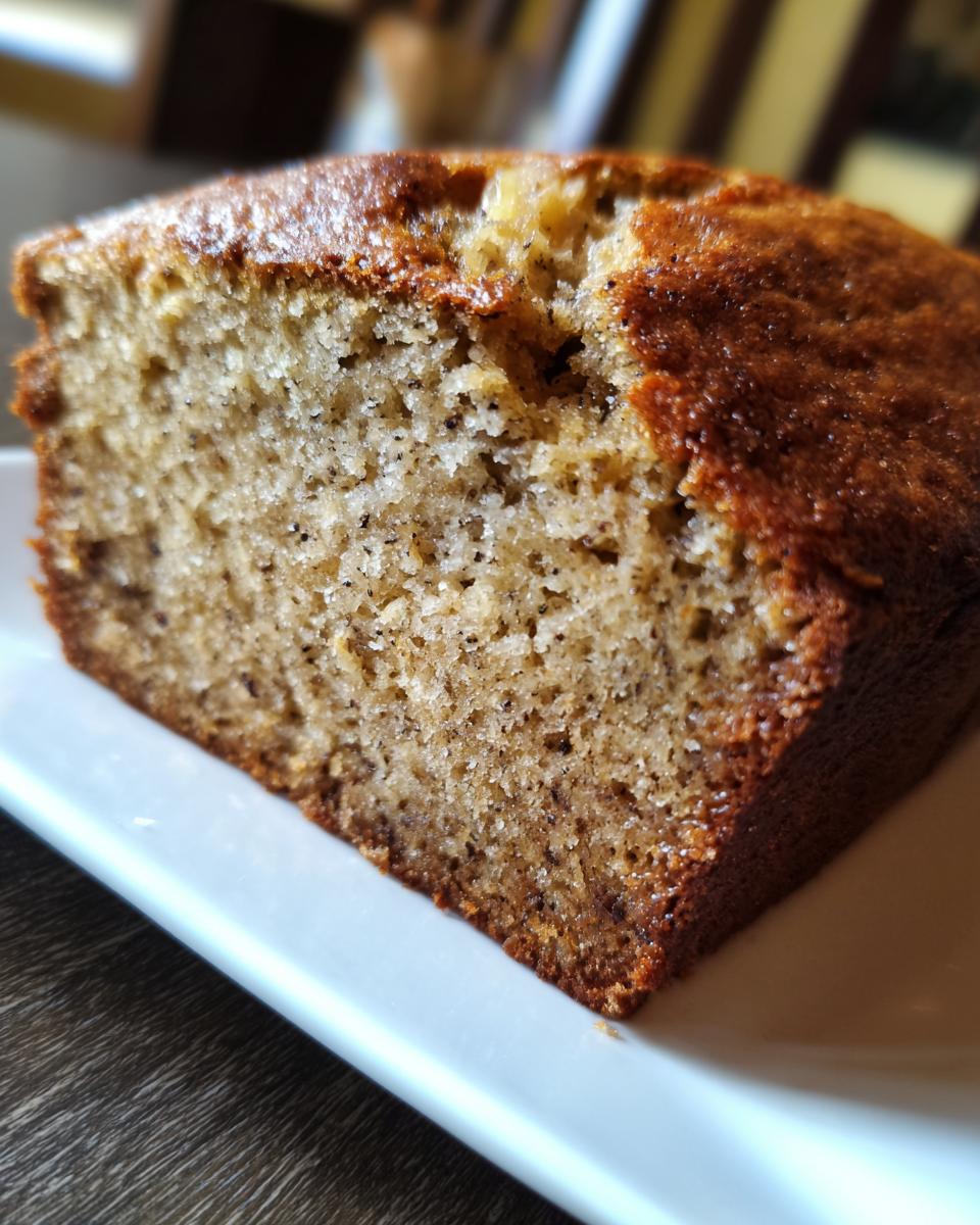 A close-up cross-section view of a slice of moist banana bread, showing the crumb texture and dark banana flecks from this banana bread recipe.