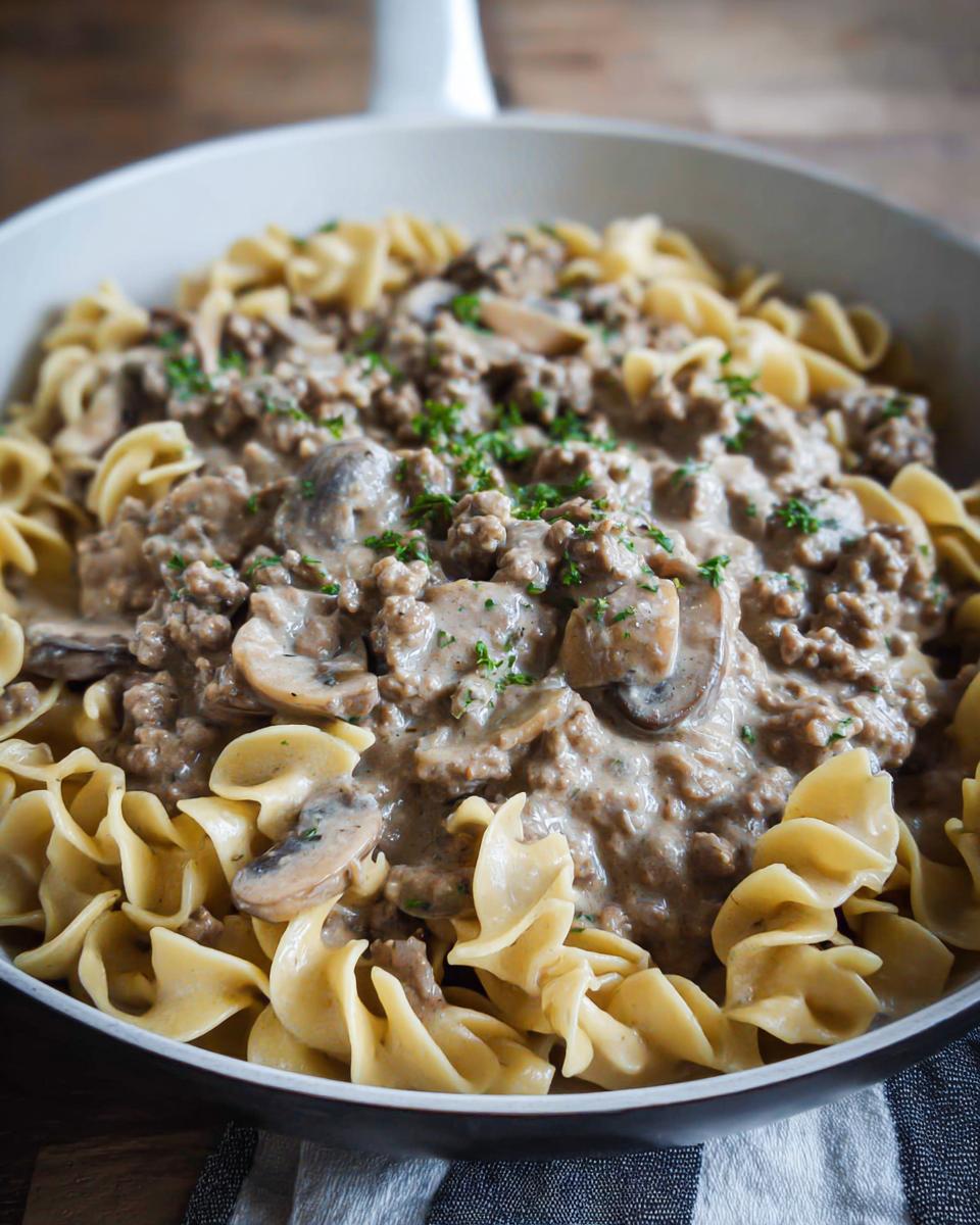 Close-up of creamy Ground Beef Stroganoff served over wide egg noodles in a white skillet.