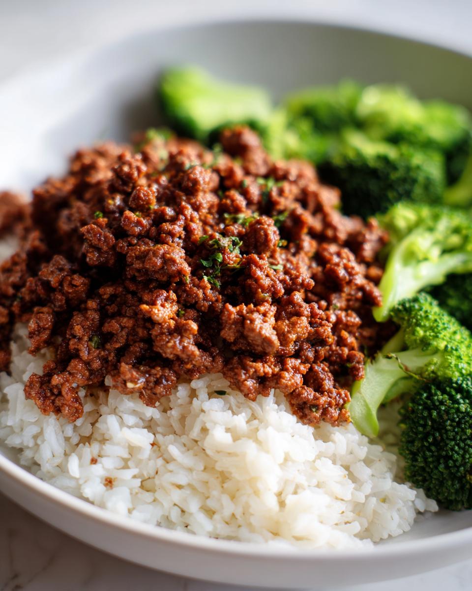 A close-up of a healthy ground beef recipes serving over white rice with steamed broccoli florets on the side.