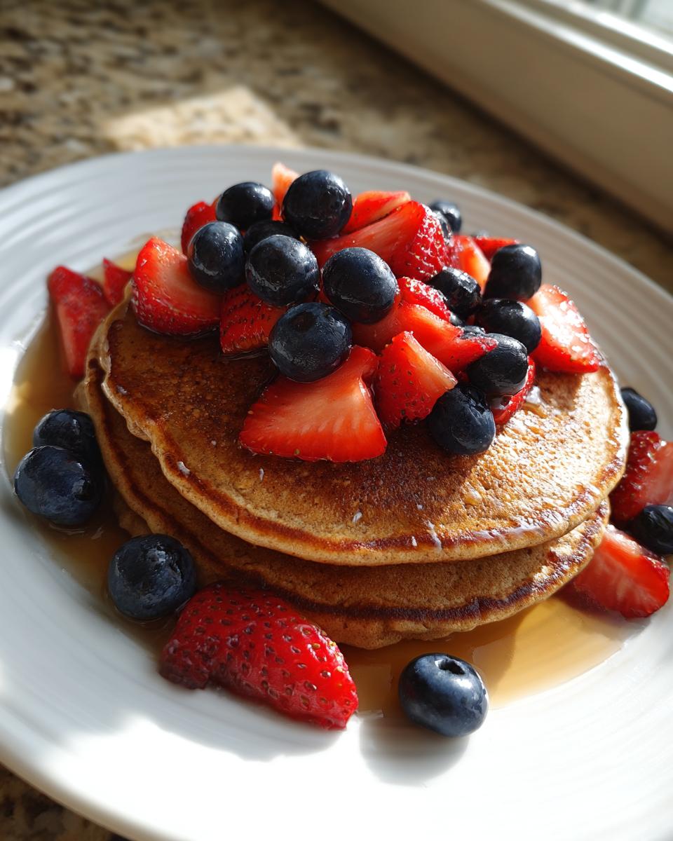 Stack of healthy pancakes topped with fresh strawberries and blueberries, drizzled with syrup, perfect for Healthy Valentine’s Breakfast Ideas.