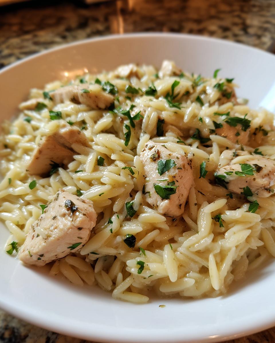Close-up of a white bowl filled with Lemon Herb Chicken Orzo Skillet, topped with fresh parsley.