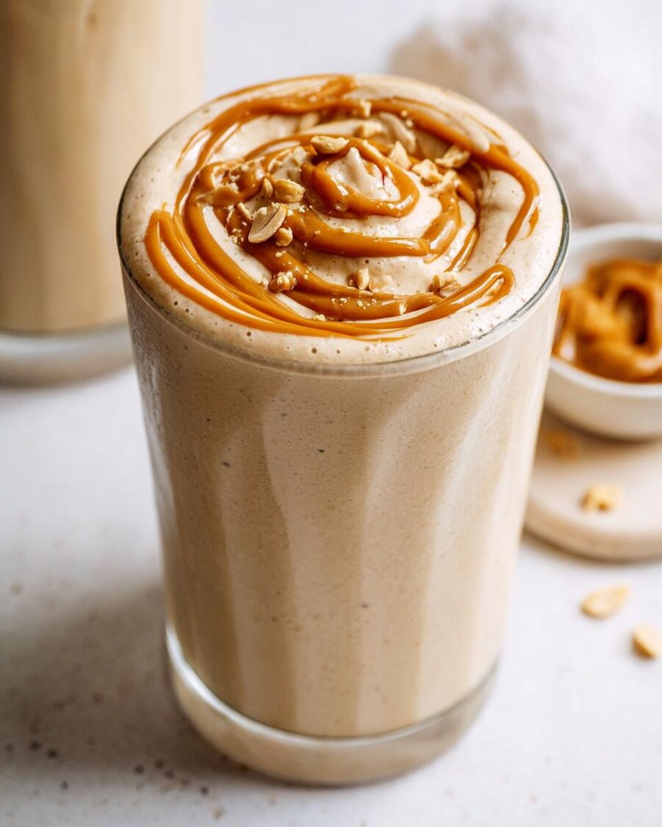 Close-up of a thick Peanut Butter Protein Smoothie topped with a swirl of caramel sauce and chopped peanuts.