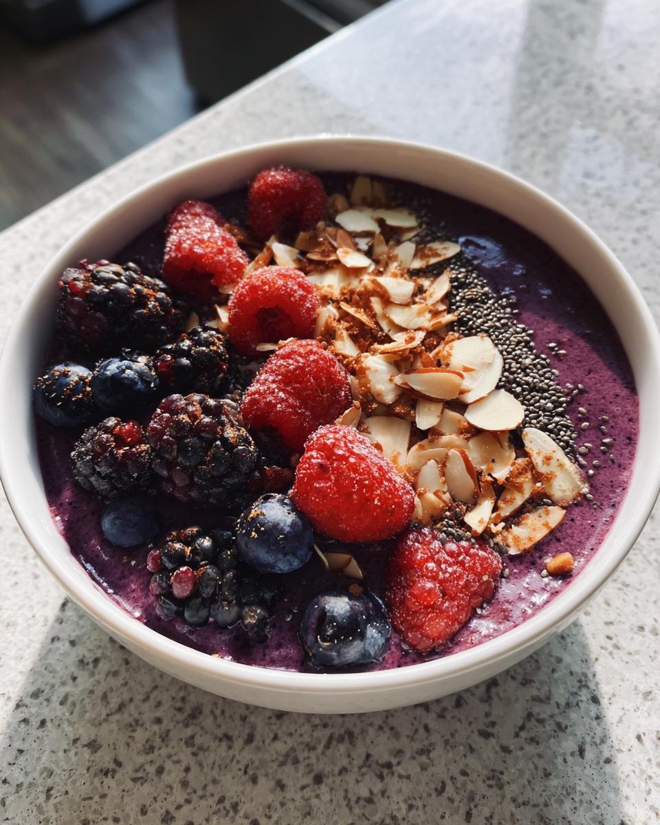 A vibrant Protein-Packed Smoothie Bowl topped with fresh raspberries, blackberries, blueberries, sliced almonds, and chia seeds.