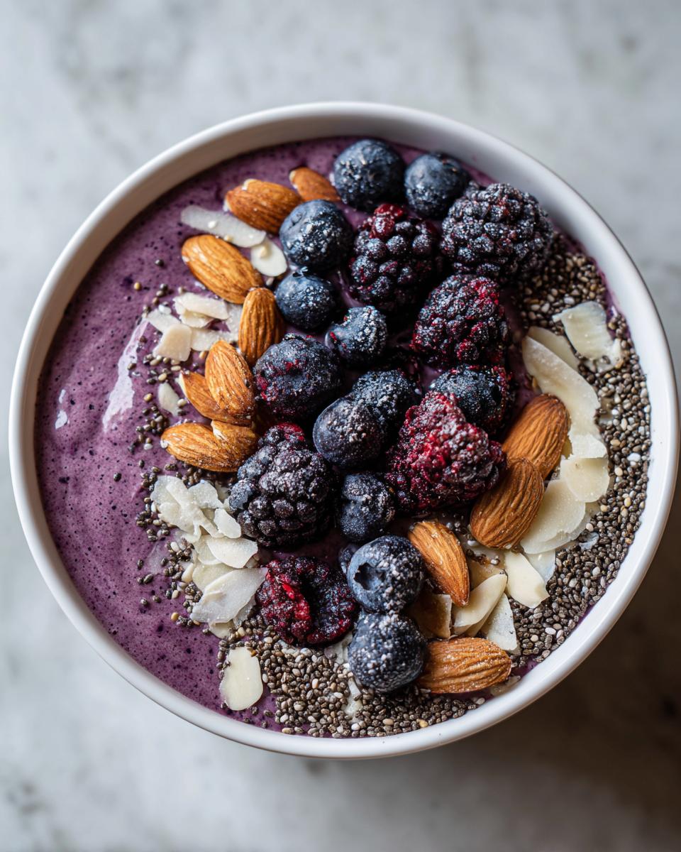 Overhead view of a vibrant Protein-Packed Smoothie Bowl topped with frozen berries, almonds, chia seeds, and coconut flakes.