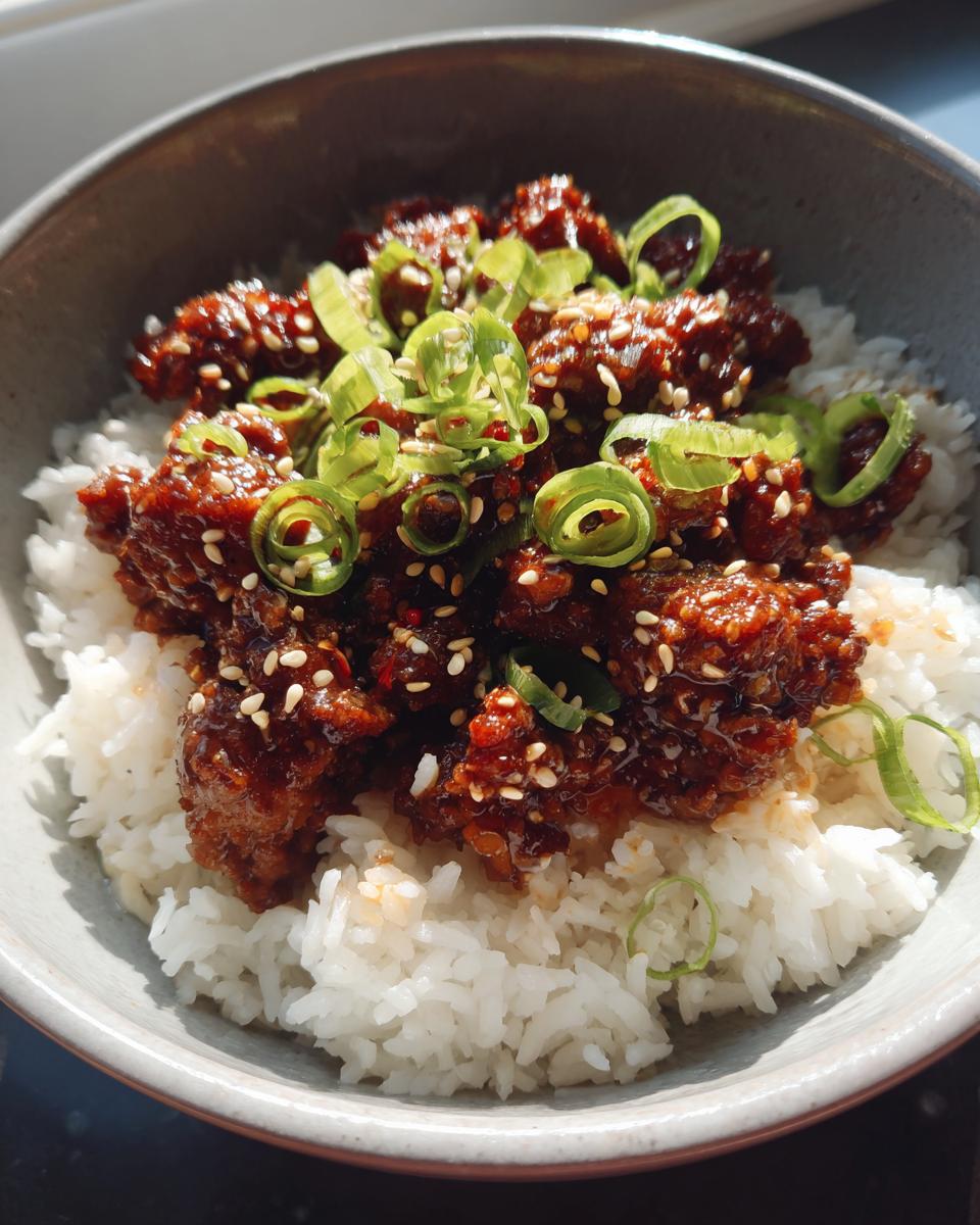 A close-up of a Quick & Easy Korean Ground Beef Bowl served over steamed white rice, topped with sesame seeds and green onions.