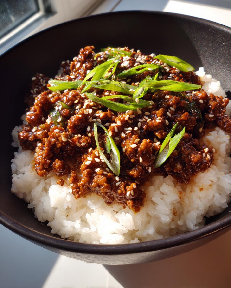 A close-up of a Quick & Easy Korean Ground Beef Bowl served over white rice, topped with sesame seeds and sliced green onions.