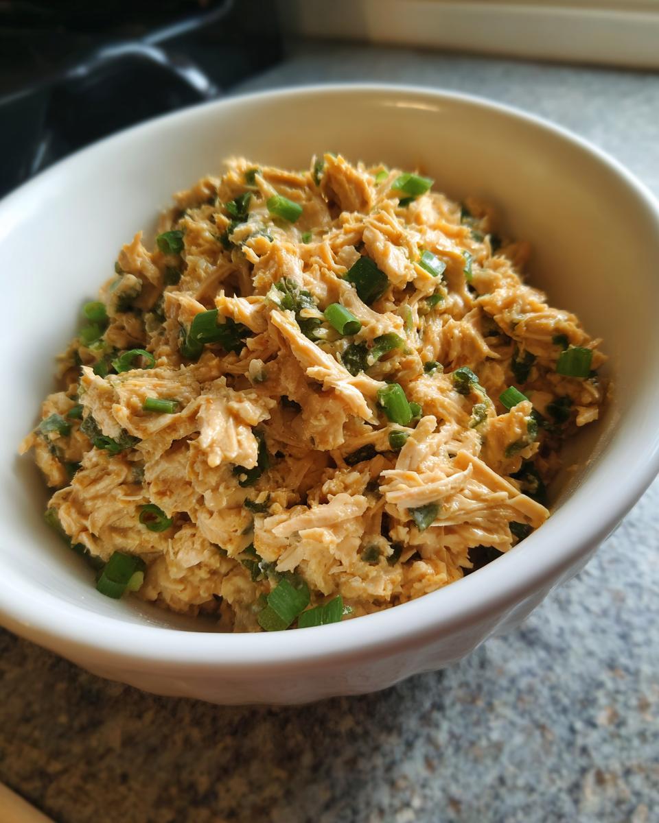 Close-up of shredded chicken salad mixed with sauce and topped with green onions, perfect for dorm-friendly easy dinner recipes.