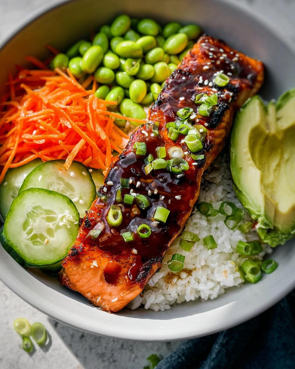 Close-up of a Teriyaki Salmon Bowl featuring glazed salmon over rice with edamame, shredded carrots, cucumber, and avocado.