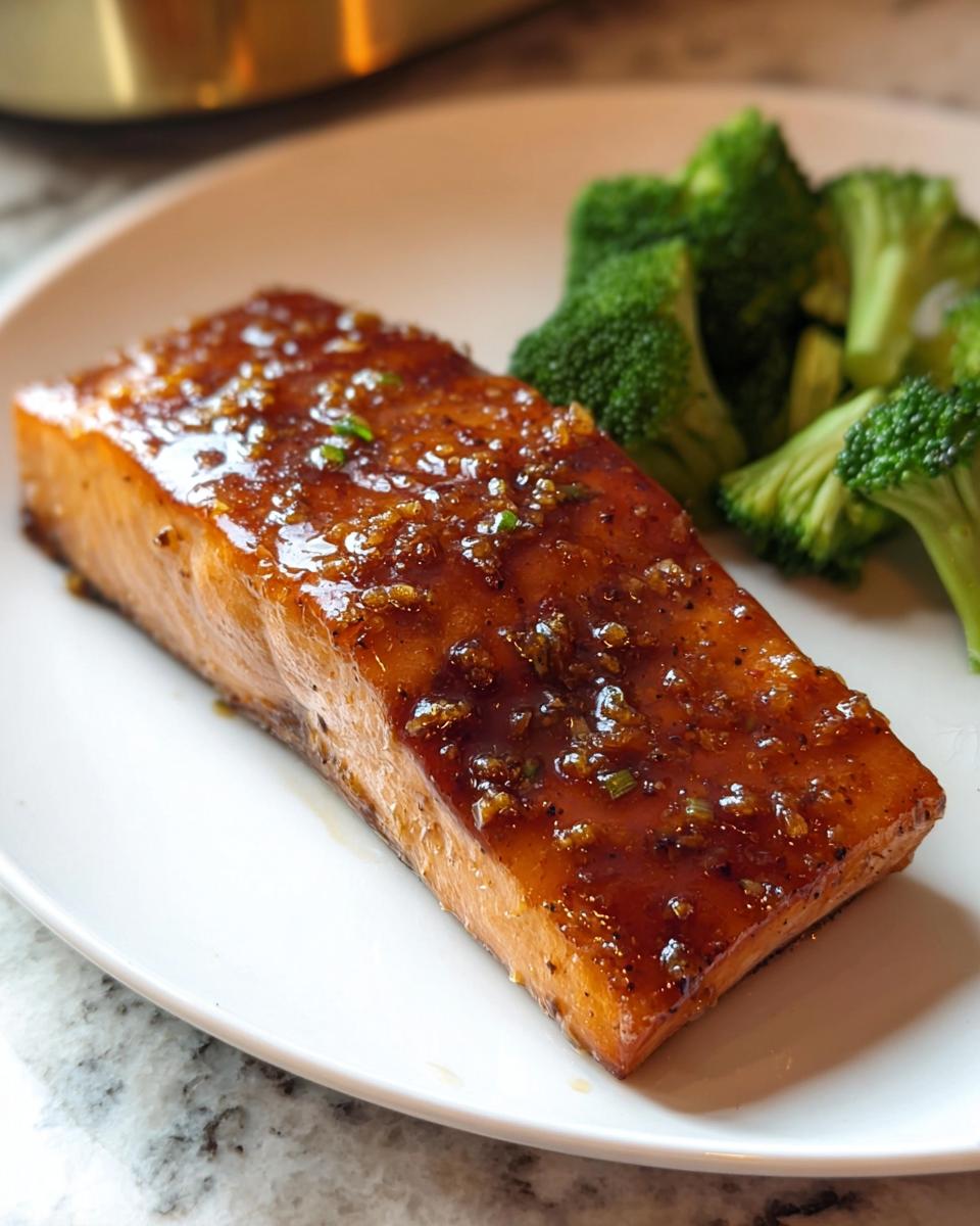 A perfectly cooked piece of healthy baked salmon recipe, glazed and served with steamed broccoli.