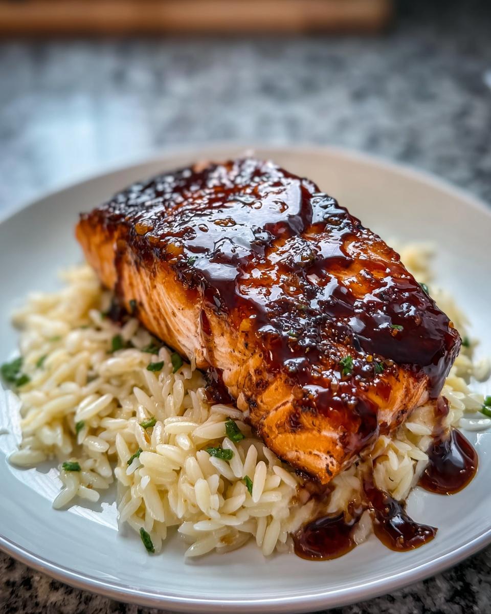 A perfectly cooked fillet of Hot Honey Salmon glazed with a dark sauce, served over a bed of orzo pasta.