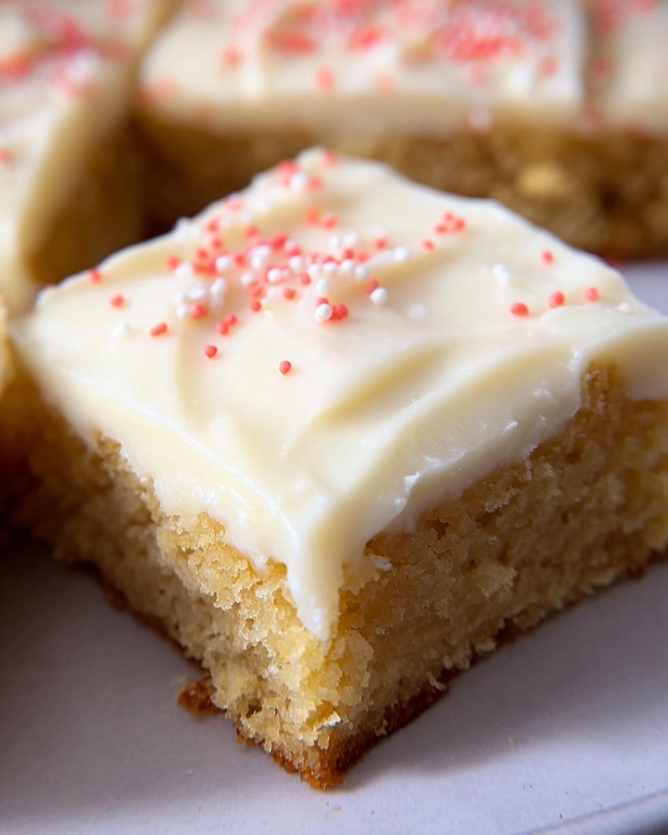 A close-up of one square of Almond Flour Sugar Cookie Bars topped with thick white frosting and red/white sprinkles.