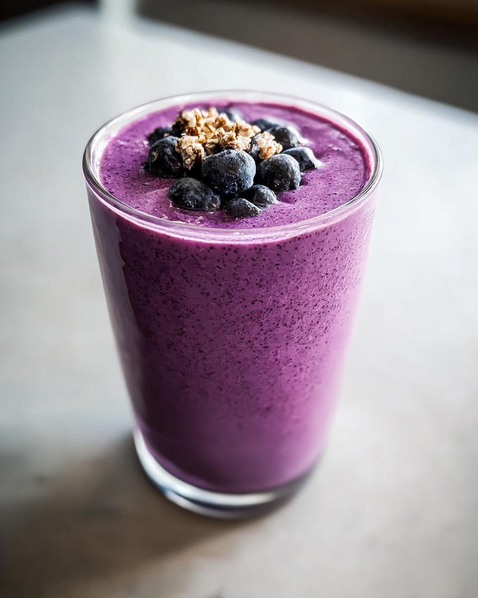 Close-up of a vibrant purple Blueberry Smoothie with Yogurt and Honey, topped with fresh blueberries and granola.