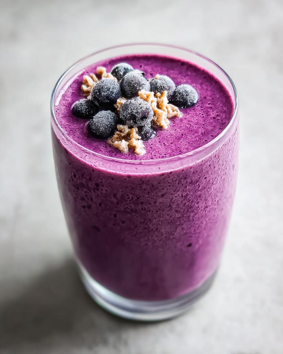 Close-up of a vibrant purple Blueberry Smoothie with Yogurt and Honey, topped with frozen blueberries and walnuts.