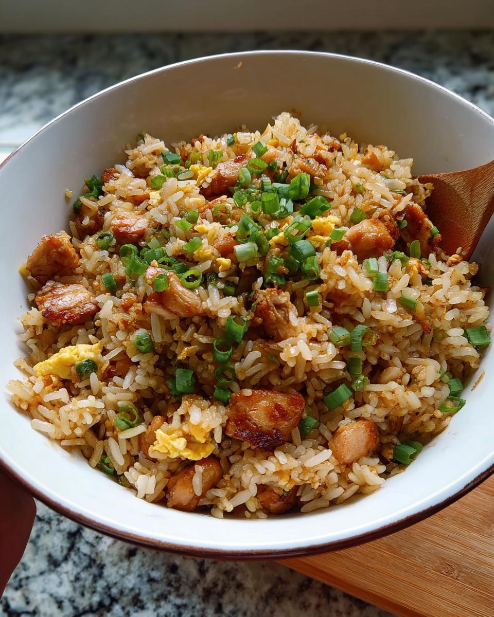 A close-up of Chicken Fried Rice with Extra Crispy Bits, topped with fresh green onions, served in a white bowl.