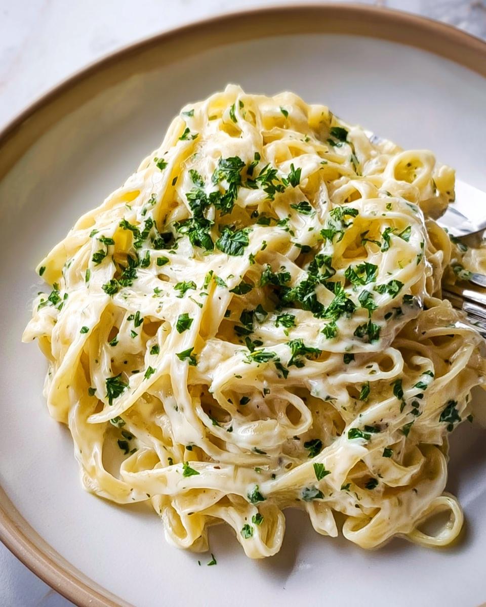 Close-up of fettuccine pasta coated generously in rich, Creamy Alfredo Sauce for Any Pasta, topped with fresh parsley.
