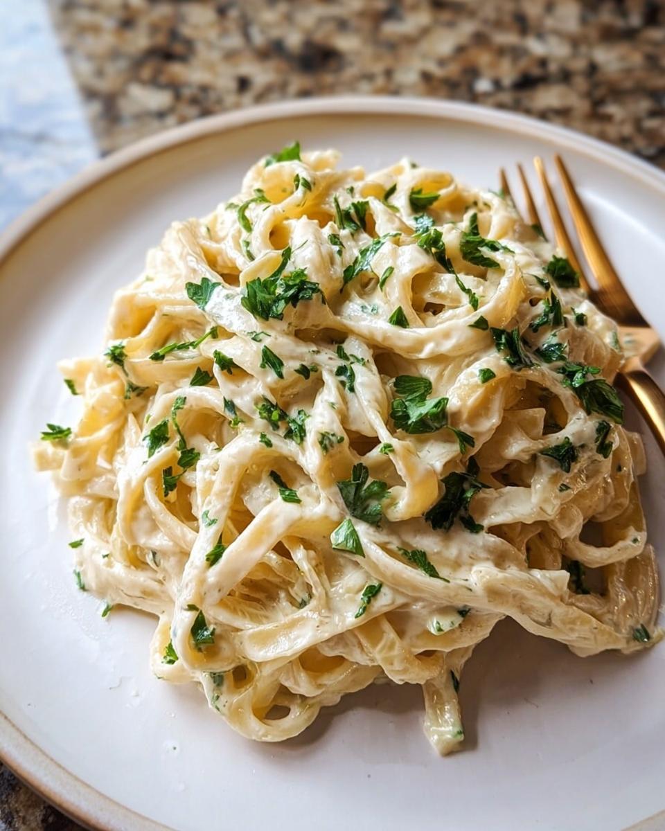 A plate of fettuccine pasta coated in rich Creamy Alfredo Sauce for Any Pasta and topped with fresh parsley.