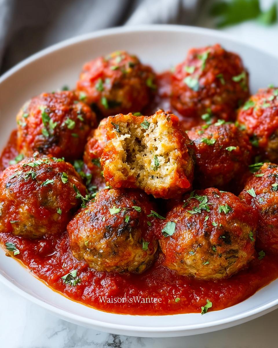 Close-up of Juicy Turkey Meatballs with Italian Herbs covered in marinara sauce, one meatball is broken open.