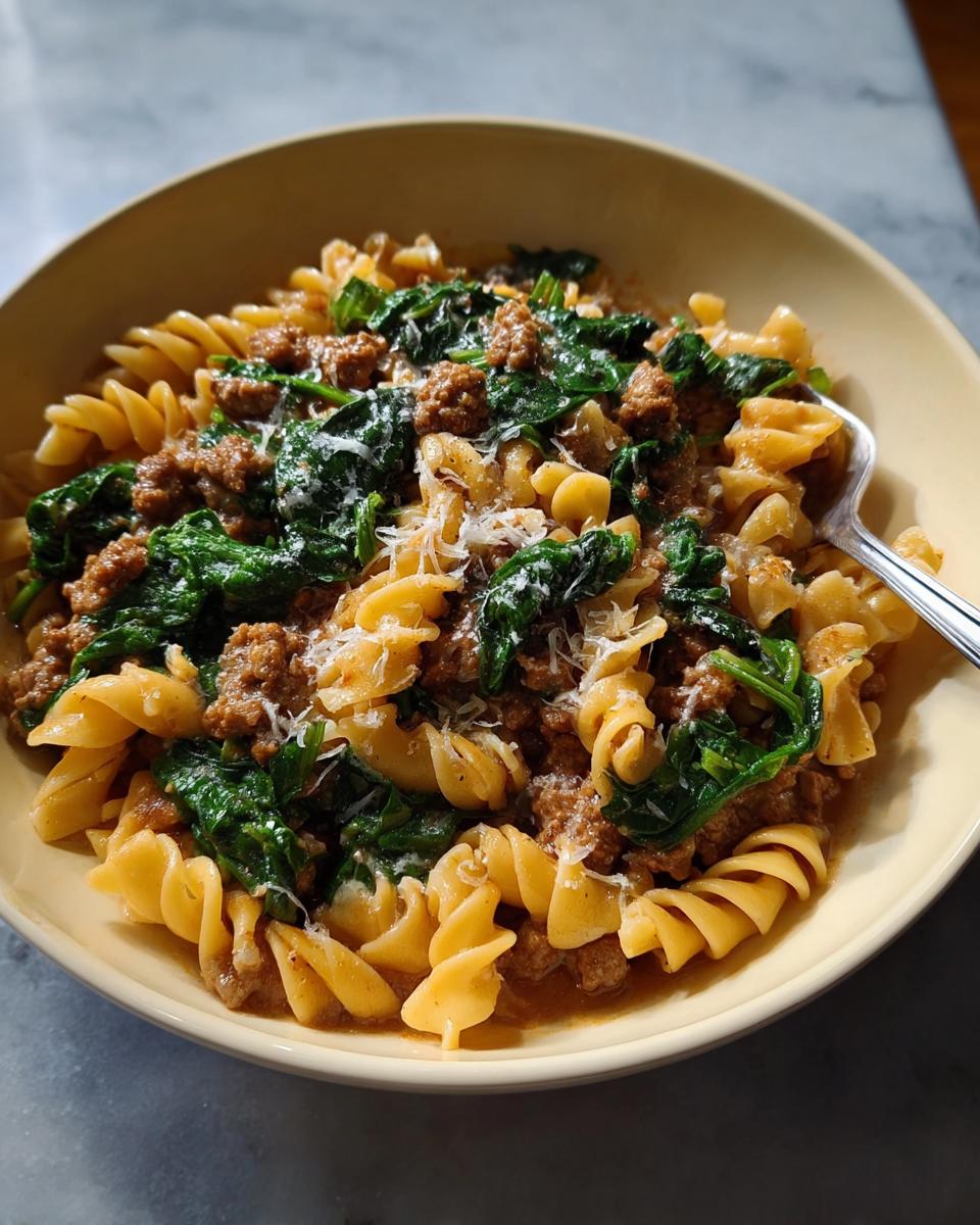 A bowl of delicious 1-Pot Pot Pasta with Sausage and Spinach topped with grated cheese.