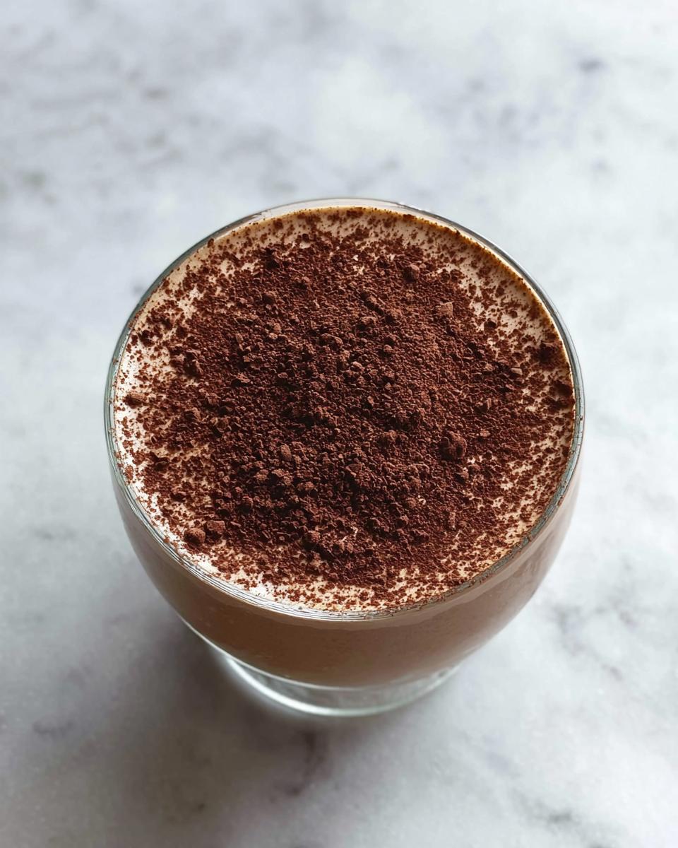 Overhead view of a glass containing finished Protein Coffee Jell, heavily dusted with dark cocoa powder.